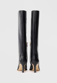 Bottes en cuir noires à hauteur de genou, avec une texture lisse, des talons hauts élancés et une fermeture éclair sur le côté agrémentée de détails en métal doré.