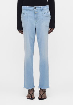 Svetlomodré rifle s rovnými nohavicami a ošúchanými lemami, nosené s čiernymi sandálmi s remienkami a čiernym dlhým tričkom.