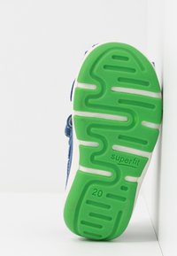 Lasten lenkkari, jossa on sininen kangasyläosa, vihreä kumipohja, joka sisältää aaltoilukuviota, ja valkoisia yksityiskohtia. Koko 20 merkitty pohjaan.