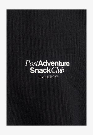Black fabric with ribbed texture featuring white embroidered text: "Post Adventure Snack Club REVOLUTION™." Simple and modern design.