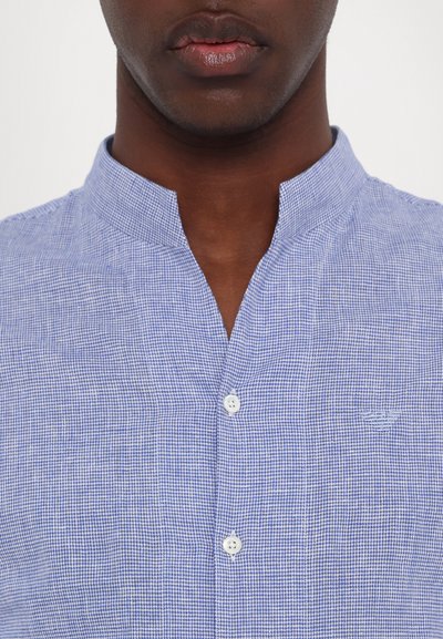 Camicia a quadri blu e bianchi con colletto alla coreana, caratterizzata da un piccolo logo sul lato sinistro e bottoni bianchi. Tessuto leggero.