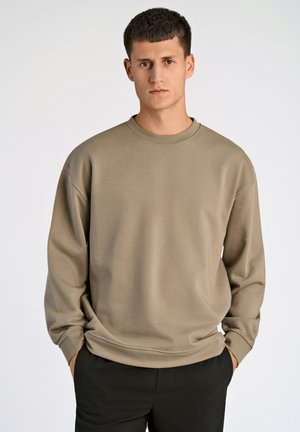 Beige Sweatshirt mit Rundhalsausschnitt und langen Ärmeln. Weicher, strukturierter Stoff; lockere Passform; über dunklen Hosen getragen. Minimalistisches Design.
