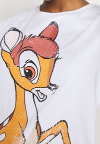 T-shirt med tryck i bomull, med en tecknad hjort i orange och brunt på en vit bakgrund, med slitna detaljer.