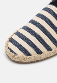Espadrille with a navy and cream striped canvas upper, braided jute trim, and a flat rubber sole. Textured fabric provides a casual look.