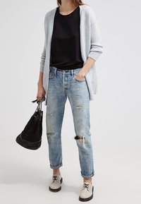 Jasnoszary, dziewiarski kardigan, czarna bluzka, zniszczone jasnoniebieskie dżinsy, czarna torebka oraz szare, sznurowane buty z czarnymi podeszwami.