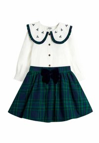 Weißes langärmliges Kleid mit großem Kragen, bestickten Schleifen und einem Rock aus marineblauem Karomuster, der eine geraffte Taille und einen Samtschleifenakzent hat.