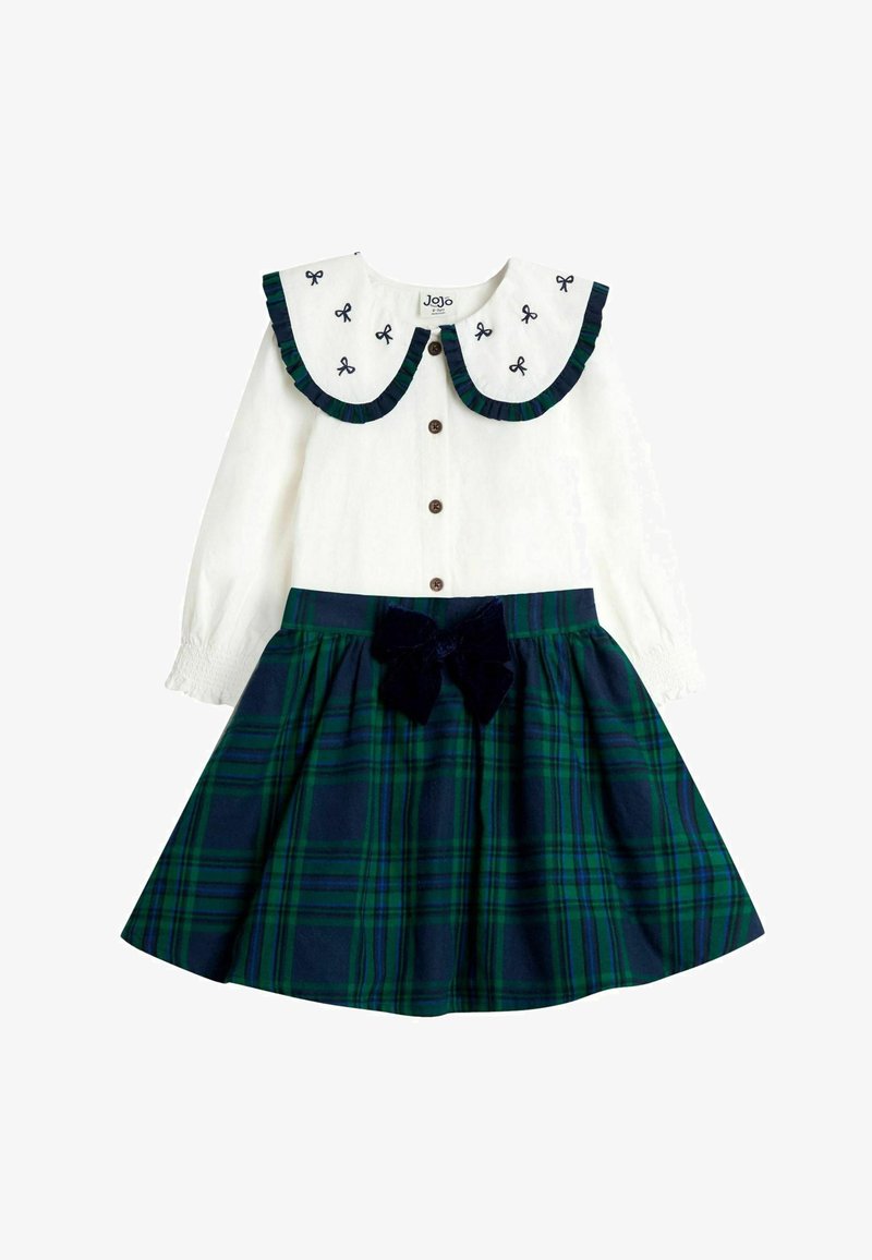 Valge pika varrukaga kleit suure kaelusega, välja paisutatud lipsudega ning tumesinise ruudulise seeliku, millel on kokkutõmmatud vöökoht ja sametist lipsu aktsent.