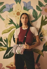 Piccola borsa a tracolla rosa con dettagli neri, decorata con strisce verdi e bianche e pois. Tracolla regolabile, tenuta da una persona.