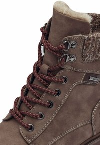 Bottine en daim marron avec des lacets en cuir tressés bordeaux, œillets en métal, doublure en fausse fourrure douce et une partie supérieure texturée avec un label DUOTEX.