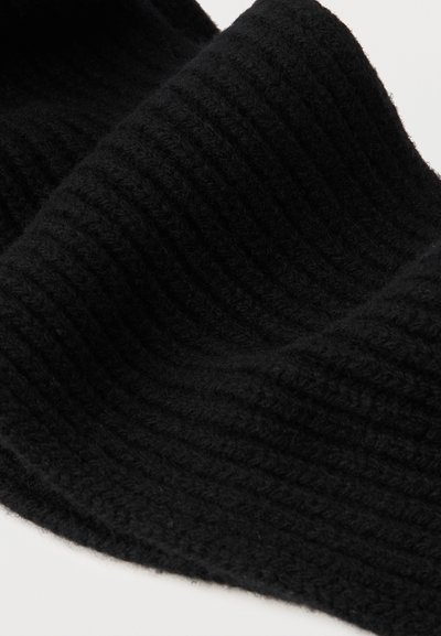 Svart stickat tyg med en ribbad struktur, draperat i mjuka veck som framhäver dess tjocka och mysiga utseende.