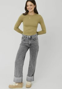 Haut à manches longues olive associé à un jean gris taille haute à jambes larges. Les jeans présentent un ourlet retourné. Les chaussures sont beiges avec un design à lacets.