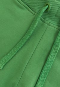 Grüne Jogginghosen mit einem strukturierten elastischen Bund und passenden Kordeln. Glatter Stoff mit verstärkten Nähten und seitlichen Paneel-Details.