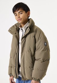 Chaqueta de plumas verde oliva con un cuello alto, cierre de cremallera y botones a presión. Presenta un parche de marca en la manga izquierda. Corte casual.