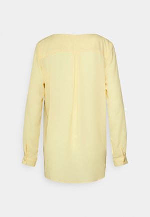 Blouse jaune clair à manches longues avec poignets à boutons, empiècement au dos et pli central dans le dos pour plus de détail.