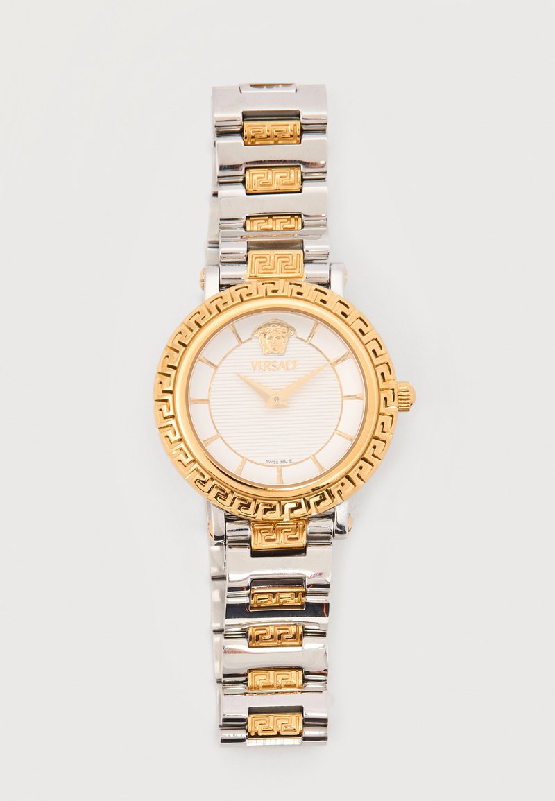 Reloj de pulsera de lujo redondo en plata y oro con bisel y correa con diseño, esfera blanca, manecillas doradas y logo de Medusa a las 12 en punto.