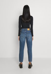 Högmidjade blå denimjeans med tapered ben, ljus tvättgradient, två bakfickor och en brun etikett vid midjan.