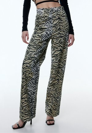 Femme portant un pantalon taille haute à jambes larges imprimé zèbre, des sandales noires à talons aiguilles et un haut court noir à manches longues.