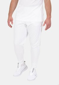 Weiße Sporthosen mit schlanker Passform, aus dehnbarem Stoff gefertigt, kombiniert mit passenden weißen Sneakers mit grauen Akzenten.