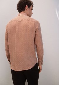 Camicia a maniche lunghe in terracotta con motivo a rombi bianchi, dotata di colletto e polsini con bottoni, realizzata in tessuto leggero.