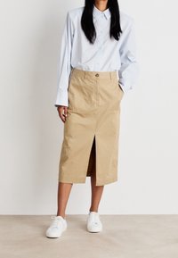 Kaki Midi-Rock mit vorne Schlitz, kombiniert mit einem hellblauen Hemd und weißen Sneakers. Aus Baumwollstoff, l�ässiges Design, praktische Taschen.