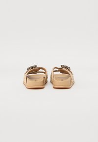 To par bakfra sandaler som har et vevd stråaktig materiale, beige farge, åpen design, flat såle og dekorativ spenne.