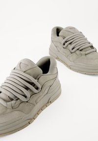 Ljusgrå sneakers med nubuckfinish, tjocka snören och strukturerad sula. Rundad form med lagerdesign och minimala varumärkesaccenter.