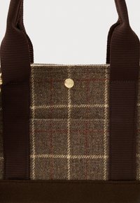 Τσάντα από ύφασμα tweed με καφέ λουράκια, μπεζ και κόκκινο σχέδιο καρό και λεπτομέρεια με κούμπωμα σε χρυσό τόνο.