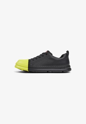 Zapatillas de cuero negro con una brillante puntera de goma amarilla, diseño de cordones, lados texturizados y suela negra.