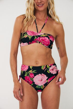 Woman wearing a black high-waisted bikini with large pink and red floral patterns and a strapless bandeau top with a halter tie.