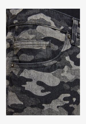 Tessuto in denim camouflage nero e grigio che presenta un primo piano di una tasca, con cuciture visibili e un dettaglio di bottone metallico argento.