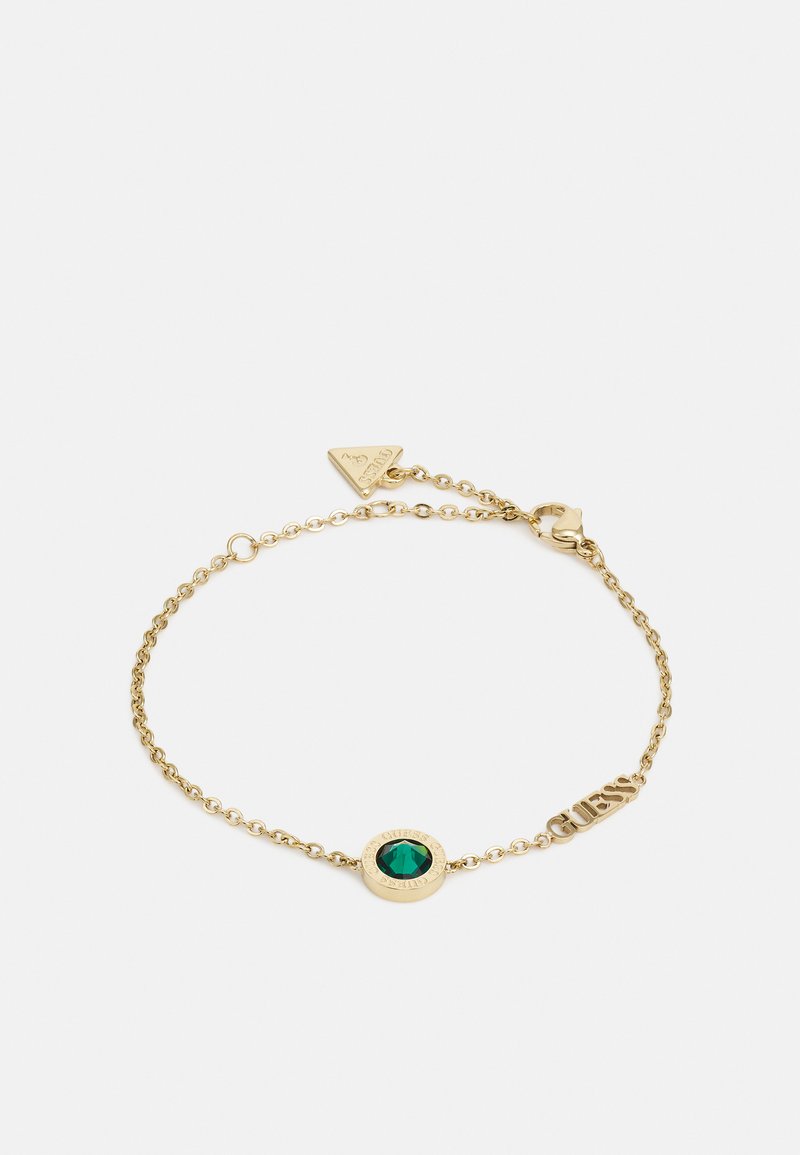 Bracciale in catena d'oro con un centrale in pietra verde, dettagli hardware incisi e un'etichetta triangolare del marchio al fermaglio.