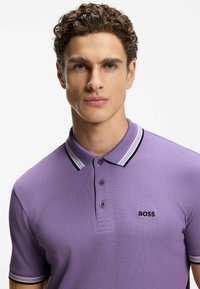 Polo viola in tessuto strutturato, con colletto a righe bianche e nere, chiusura a tre bottoni e logo "BOSS" ricamato.