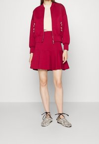 Magenta bomberka z haftem kwiatowym, kremowa bluzka, rozkloszowana spódnica w kolorze magenta oraz błyszczące buty na sznurówki z czarnymi wiązaniami. Gładka tekstura.