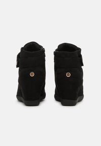 Svarta mocka anklarboots med kilklack, dragkedjestängning och justerbar rem med guldtonad detalj. Texturerad panel bak.