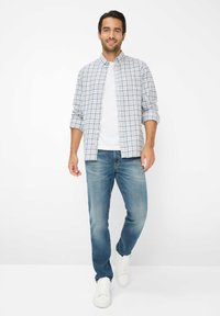 Geruite button-up-shirt in blauw en wit, gedragen over een wit T-shirt, gecombineerd met lichtblauwe jeans en witte sneakers. Casual fit.