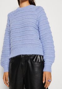 Maglione lavorato a maglia azzurro chiaro con strisce orizzontali testurizzate, scollo a girocollo e orli a coste, abbinato a pantaloni in pelle nera.