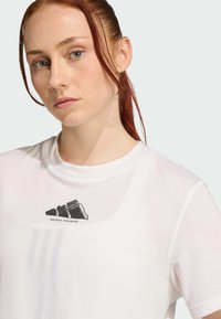 T-shirt blanc à manches courtes avec un logo graphique noir sur la poitrine, fabriqué à partir d'un matériau léger avec une texture lisse.