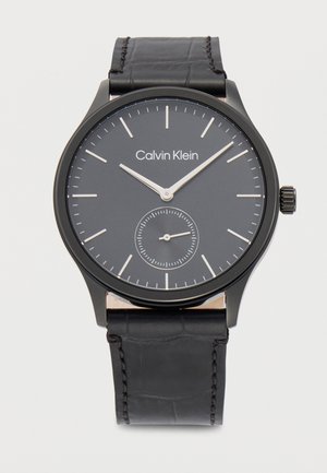 Crni sat Calvin Klein s minimalističkim brojčanikom, srebrnim kazaljkama za sate i minute, malim brojčanikom za sekunde i crnim kožnim remenom.