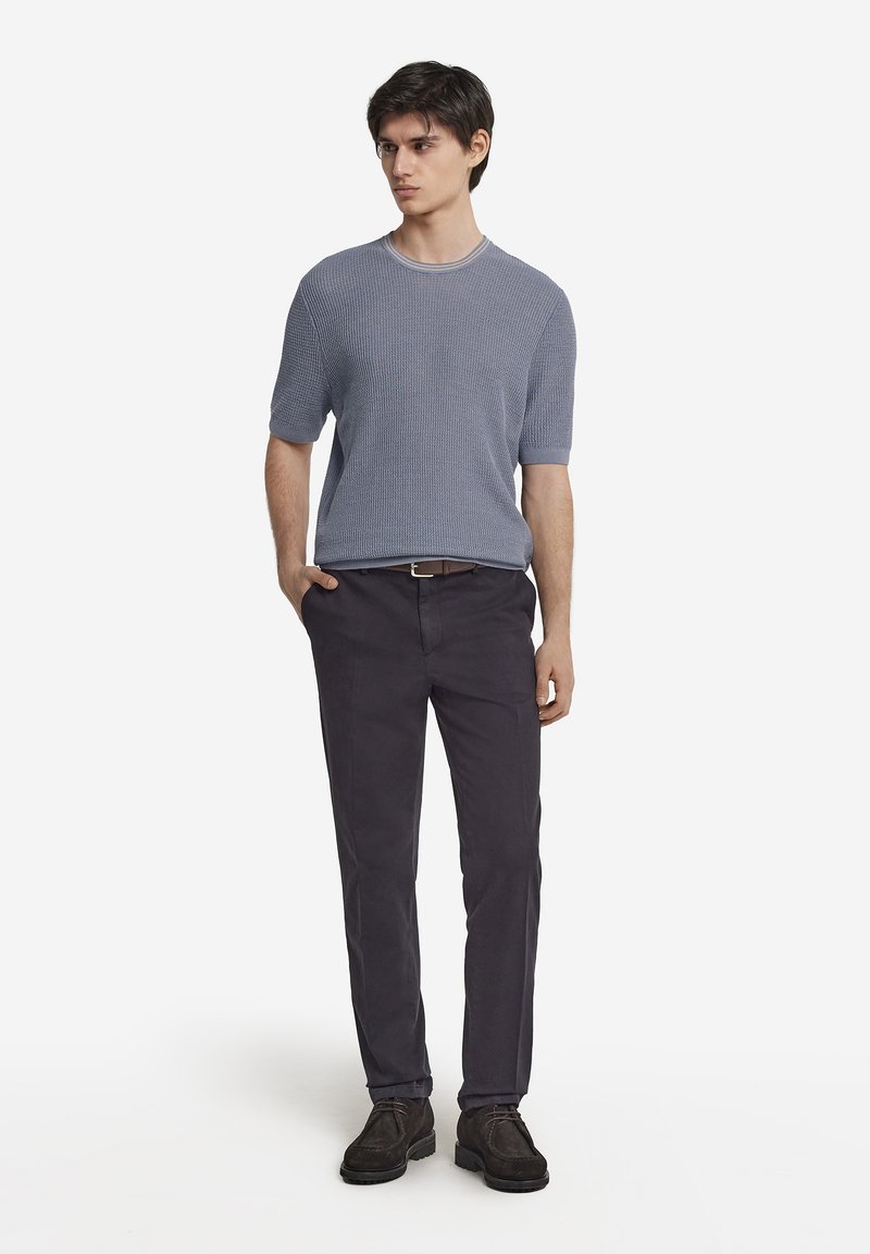 Ljusblå stickad kortärmad tröja, rakt skurna mörka byxor och bruna snörskor. Enkelt mönster och strukturerad tyg.