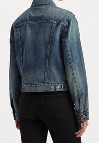 Denimjacka i medelblått, skräddarsydd design med två knappar vid fållen och en klassisk krage. Strukturerad tyg med synliga sömdetaljer.