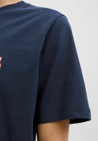 Tamsiai mėlynas medvilnės marškinėliai su trumpomis rankovėmis, apvaliu kaklu ir minkštu paviršiumi. Pabrėžia spausdintą dizainą priekyje.