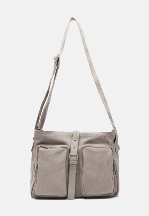 Sac d'épaule en tissu gris avec une sangle réglable, deux poches avant, une poche latérale zippée et un accent de ceinture central.