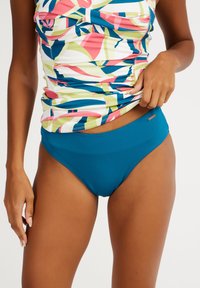 Maudymosi viršus su daugiakampiu geometriniu raštu ir susiraukšlėjimais; maudymosi kelnių apačia vienintos spalvos žalios spalvos, abu pagaminti iš tamprios medžiagos, užtikrinančios komfortą.