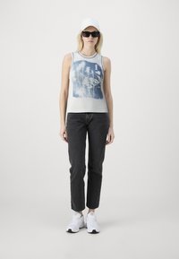 Ermeløs hvit tanktopp med blå blomstermotiv, parret med sorte straight-leg jeans og hvite treningssko. Sorte solbriller og caps inkludert.