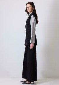 Black tailored vest with a belt, paired with a light gray shirt featuring wide sleeves, black wide-leg trousers, and pointed black heels.