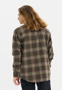 Bruine geruite blouse met een ontspannen pasvorm, lange mouwen en contrasterende beige lijnen. Voorzien van knoopmanchetten en een licht gebogen zoom.
