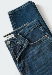 Jean en denim bleu foncé plié avec poche avant visible, bouton et fermeture éclair partiellement ouverte sur fond blanc.