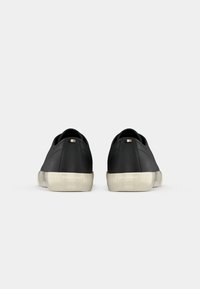 Pair of black low-top leather sneakers with white rubber soles and "BOSS" embossed on the heel, shown from the back on a white background.