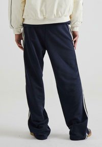 Marineblå sweatpants lavet af blødt stof, med en afslappet pasform, hvide sidestriber og et bredbenet design for komfort.