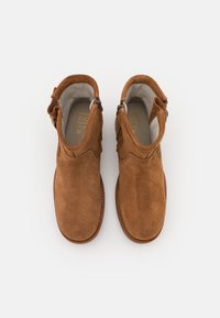 Botas cortas de ante marrón con cremallera lateral, punta redondeada y un forro interior suave. Presentan detalles cosidos y una suela plana.